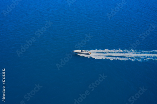 Aerial view of a boat in motion on blue water. Top view of a white boat sailing in the blue sea. Drone view of a boat sailing at high speed. © Berg