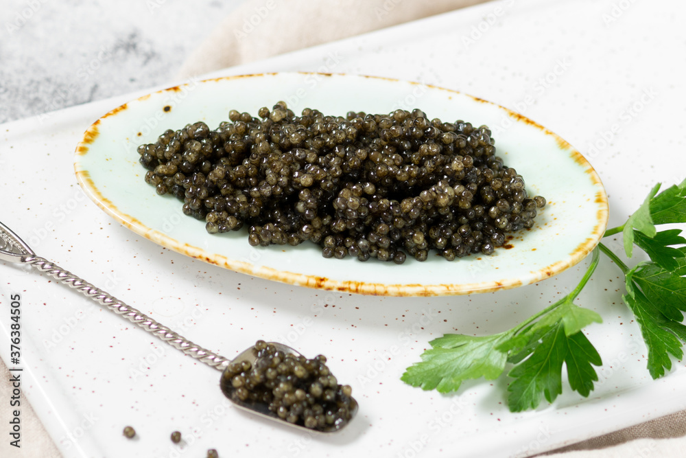 Black caviar. Black sturgeon caviar in a ceramic bowl and a metal spoon on a light background. Useful delicacy Black caviar. Black sturgeon caviar in a ceramic bowl and a metal spoon on a light background. Useful delicacy