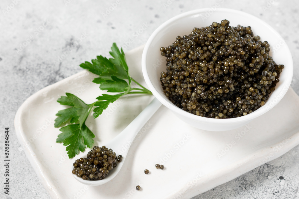 Black caviar. Black sturgeon caviar in a ceramic bowl and in a ceramic spoon on a light background. Useful delicacy Black caviar. Black sturgeon caviar in a ceramic bowl and in a ceramic spoon on a light background. Useful delicacy