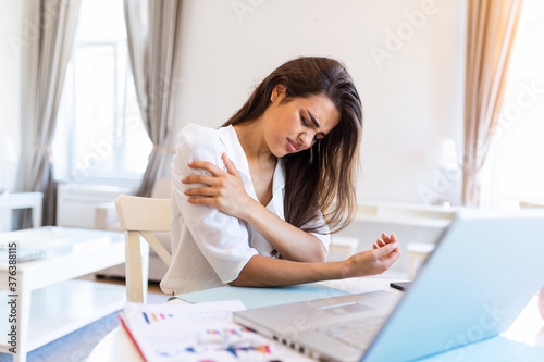 Young woman with hands holding her shoulder pain. Office syndrome and Health care concept. Business woman working with her laptop and with shoulder pain in the home office photo