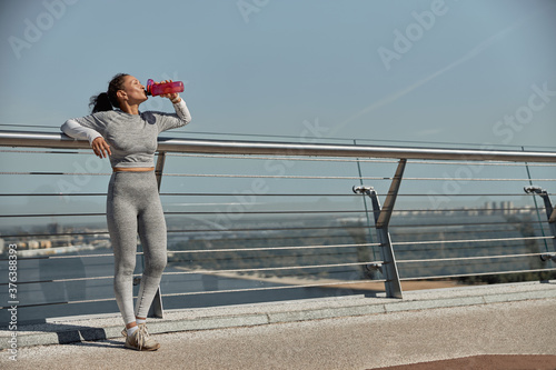 happy healthy and sporty woman is drinking water after workout trainings in sunny day