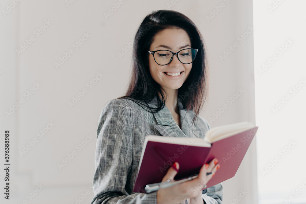 Photo of creative cheerful author thinks on writing interesting article, creats new plans, smiles happily, wears eyeglasses with good lenses, makes notes in notepad, dressed in formal clothes Photo of creative cheerful author thinks on writing interesting article, creats new plans, smiles happily, wears eyeglasses with good lenses, makes notes in notepad, dressed in formal clothes
