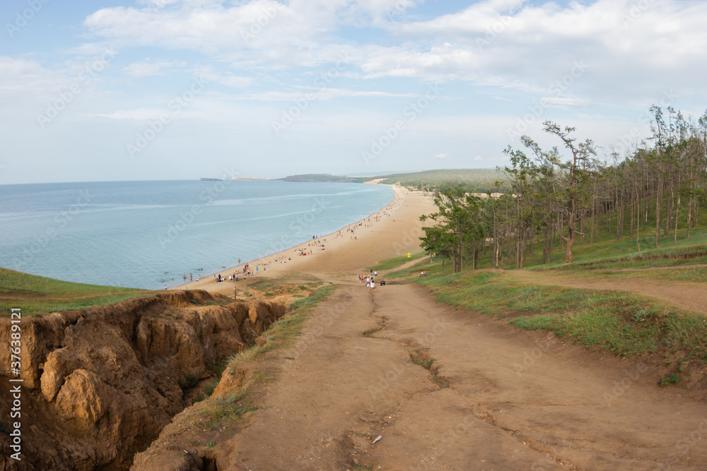 The road to the sandy beach with people on Lake Baikal, to the left of which there is a moat