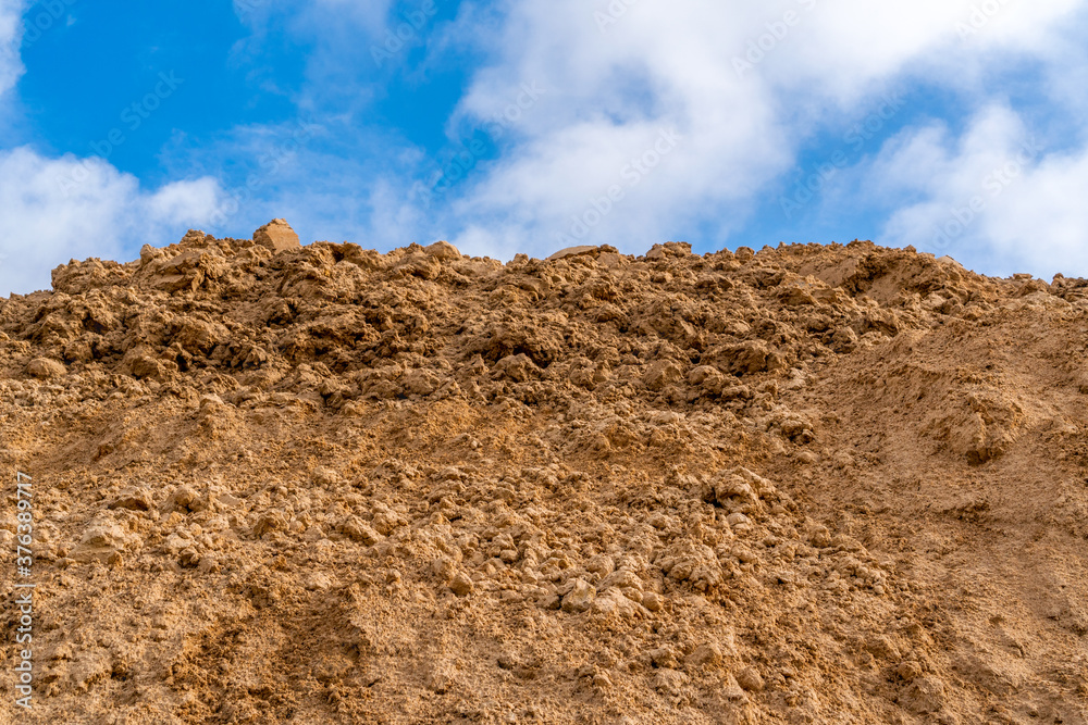 Pile of sand for construction against a blue sky with clouds