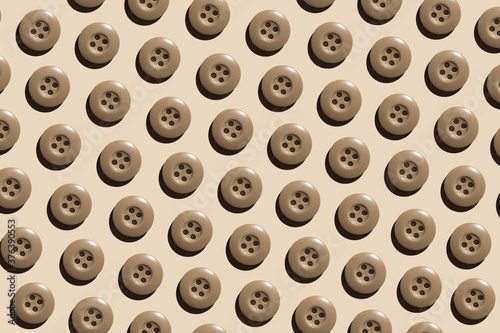 A pattern of beige round plastic buttons on a pastel beige background. The concept of needlework  sewing clothes.
