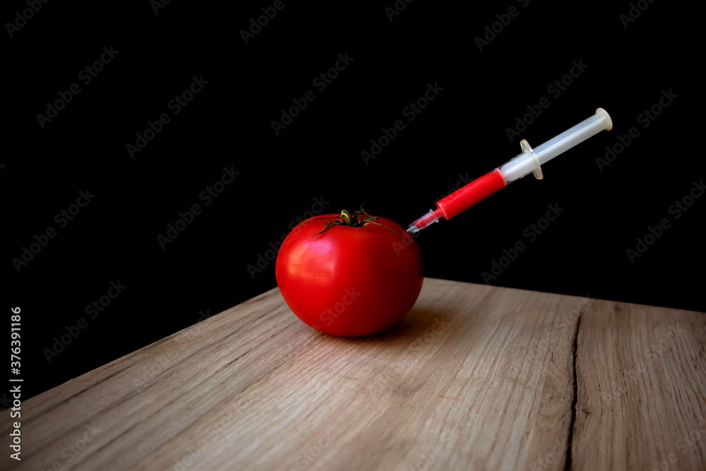 Ripe red tomato on a wooden board and syringe inside it extracting red liquid Ripe red tomato on a wooden board and syringe inside it extracting red liquid