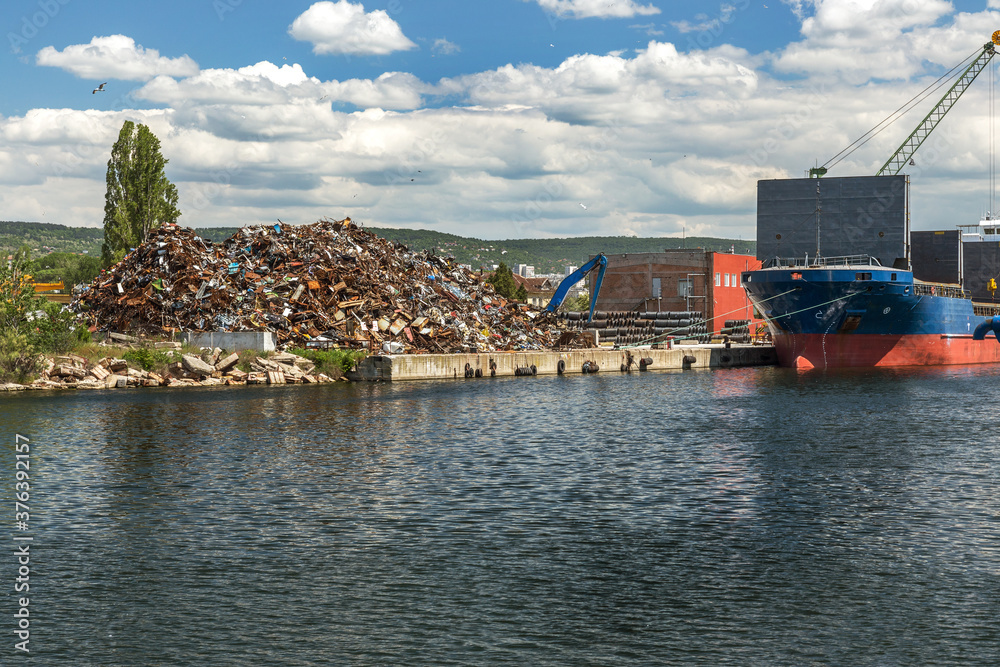 A large heap of scrap metal in the processing and loading area in sea cargo ships. A scrap heap on an industrial quay in the cargo port area is prepared for loading and transportation by sea