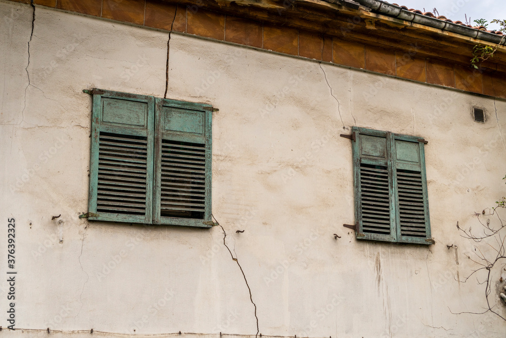 Facade of an abandoned building with old windows with green shutters