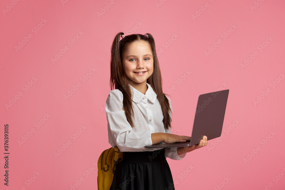 E-education. Smiling schoolgirl in uniform with backpack works on laptop E-education. Smiling schoolgirl in uniform with backpack works on laptop