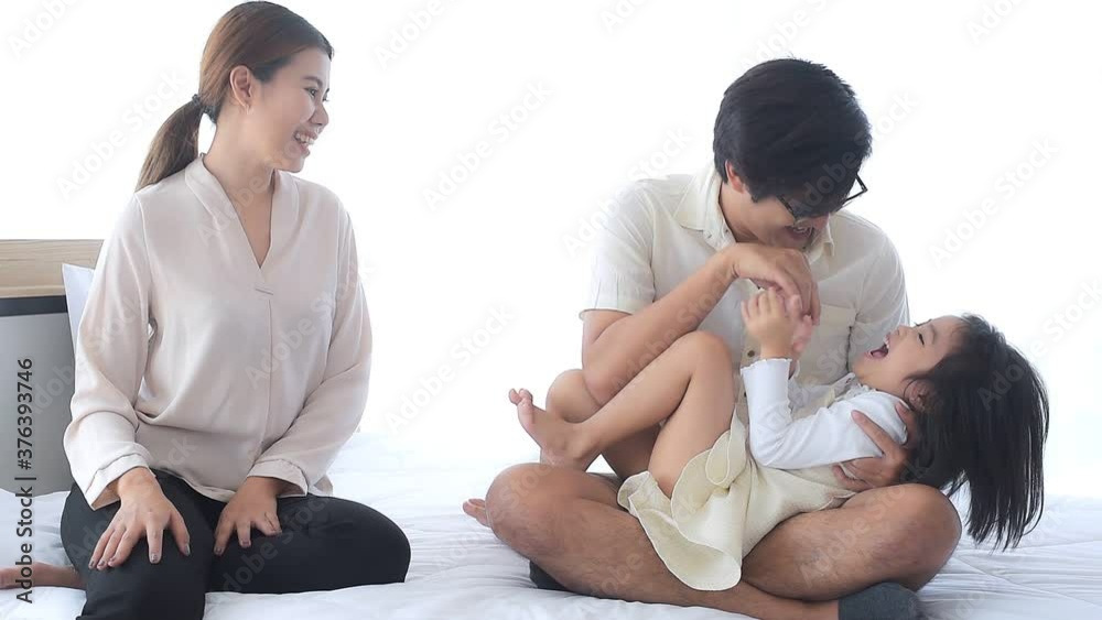Asian Parents are happily teasing her cute daughter in bed. The daughter was lying on her father's lap and was tickled for a cheerful laugh.Happy family at home concept