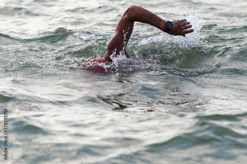 Swimmer swims in sea. Athlete triathlete swimmer drains from water. A professional athlete in triathletes trains for an ironman. The sportsman beautifully floats in blue sea water at competitions