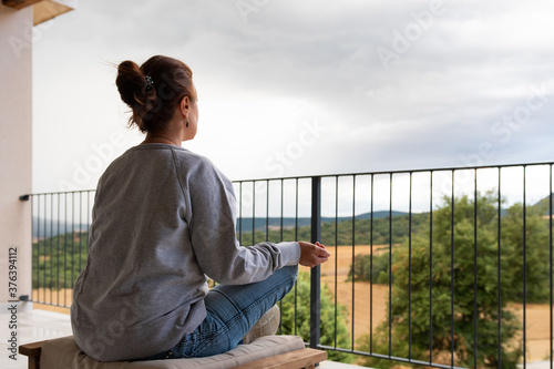 Картината върху платно Mujer sentada meditando en el balcón del hogar con las piernas recogidas y los b