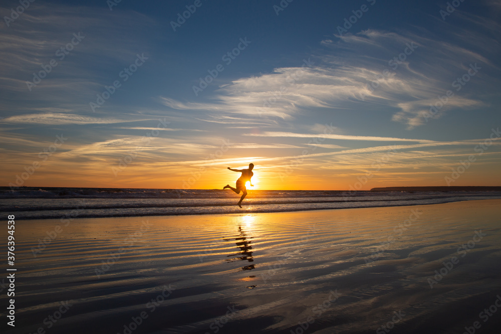 Man silhouette jumping and covering the sun in the long beach of Zahara de los Atunes in the Atlantic Ocean at sunset, Cadiz, Spain