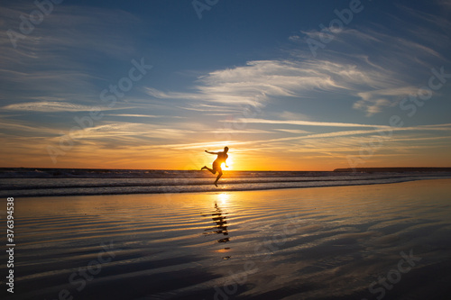 Man silhouette jumping and covering the sun in the long beach of Zahara de los Atunes in the Atlantic Ocean at sunset, Cadiz, Spain