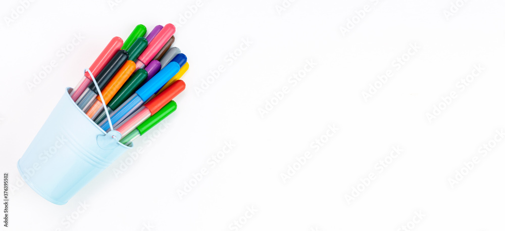 Obraz premium Set multicolored pointed markers in a light blue bucket on a white background, copy space, banner. Drawing felt-tip pens, pencils, artists tools, creativity, leisure, hobby. Colorful school supplies.