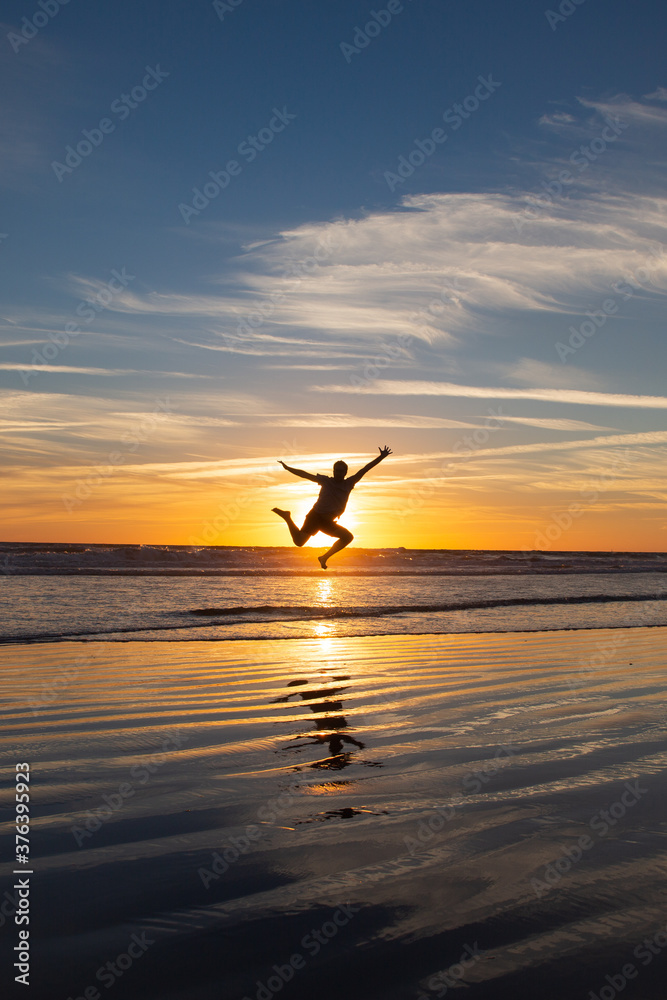 Young man jumping and covering the sun in the long beach of Zahara de los Atunes in the Atlantic Ocean at sunset, Cadiz, Spain