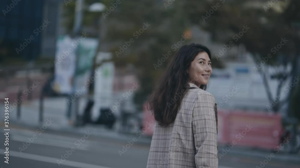 Portrait of businesslady crossing street. Young woman in business district with skyscrapers, heading to job. During the scene, girl turn head and smiling to camera. Concept of work, lifestyle. Portrait of businesslady crossing street. Young woman in business district with skyscrapers, heading to job. During the scene, girl turn head and smiling to camera. Concept of work, lifestyle.