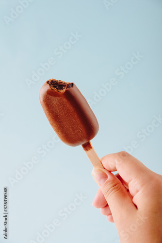 Chocolate cake in the form of ice cream on a stick on a white plate and a colored background