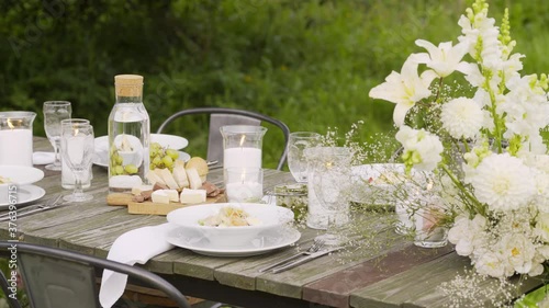 vintage wooden table with elegant festive setting and burning candles decorated with fresh white aromatic flowers stands in summer garden closeup photo