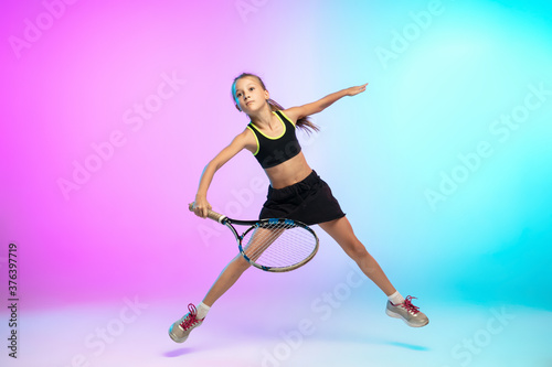 Running high. Little tennis girl in black sportwear isolated on gradient background in neon light. Little caucasian model, sport kid training in motion and action. Sport, movement, childhood concept.