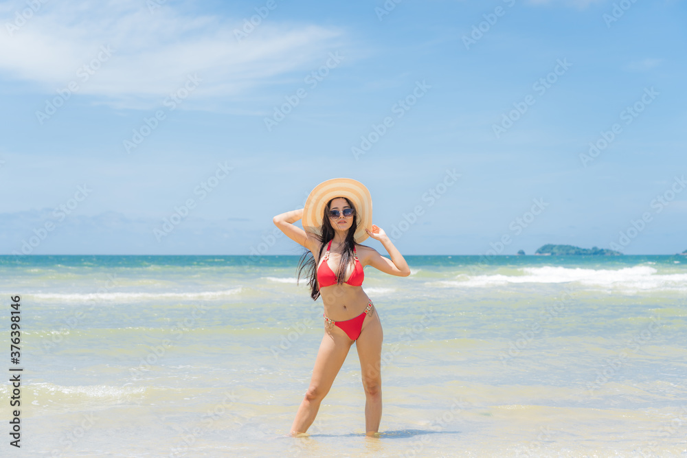 Asian woman wear a colourful bikini stand sunbathing on the sandy beach in a bright day and happy holidays with blue sky Asian woman wear a colourful bikini stand sunbathing on the sandy beach in a bright day and happy holidays with blue sky