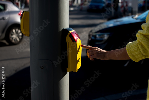 Young woman in a yellow sweater presses the button at the pedestrian crossing. A woman is standing at the crosswalk waiting for the green light. A young woman pressing the button to cross the road