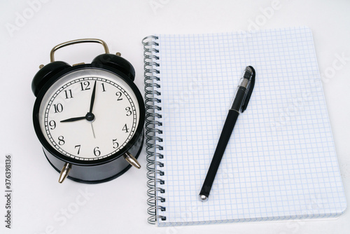 Notepad with alarm clock and pen on a white background.