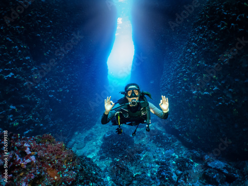 Eine Scuba Taucherin signalisiert das OK Zeichen vor einer Unterwasser Höhle im Ägäischen Meer, Griechenland
