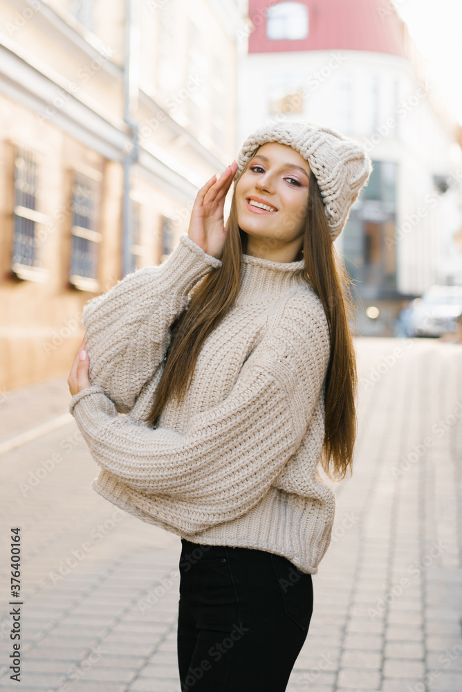 Autumn portrait: a young woman, dressed in a warm wool sweater and hat, poses on a city street and smiles Autumn portrait: a young woman, dressed in a warm wool sweater and hat, poses on a city street and smiles