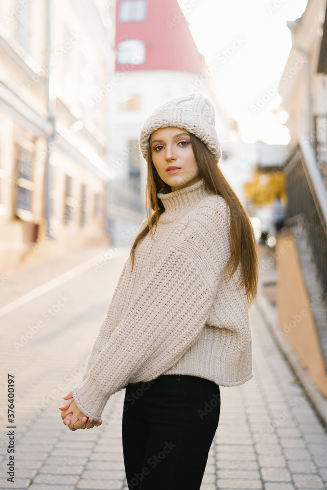 Fashionable lifestyle Portrait of a young fashionable woman dressed in a knitted warm sweater and a knitted hat, posing, I'm in the Old town, autumn street fashion.