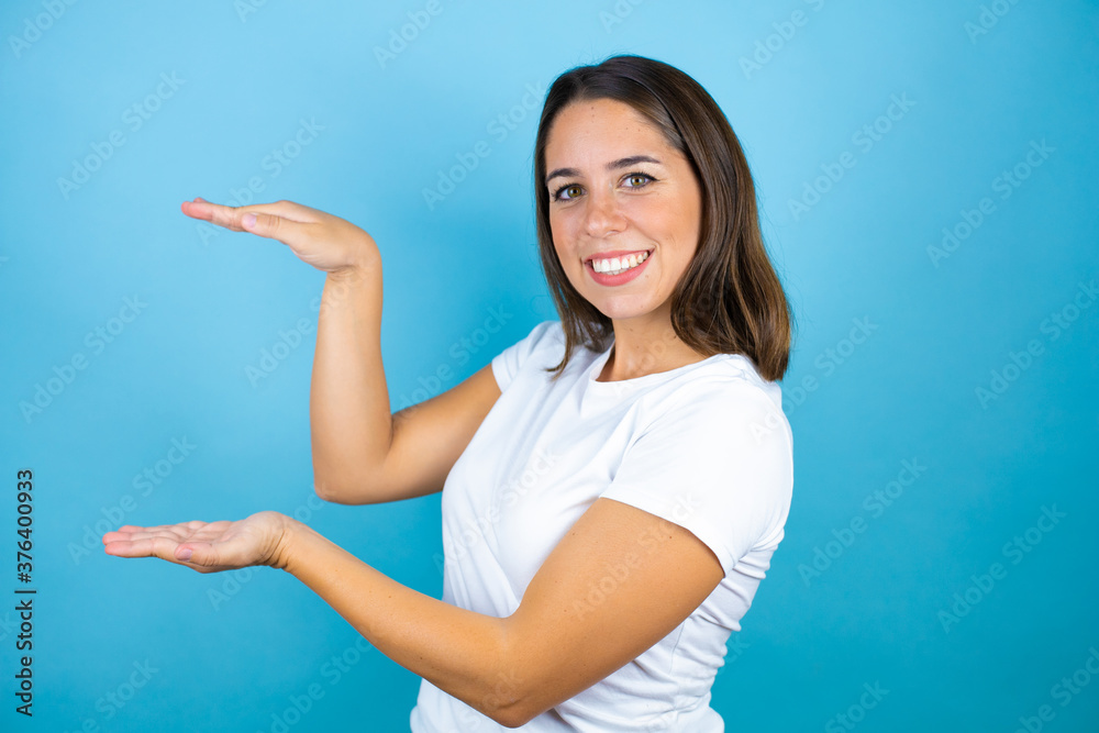 Young beautiful woman over isolated blue background gesturing with hands showing big and large size sign, measure symbol. Smiling looking at the camera. Measuring concept. Young beautiful woman over isolated blue background gesturing with hands showing big and large size sign, measure symbol. Smiling looking at the camera. Measuring concept.