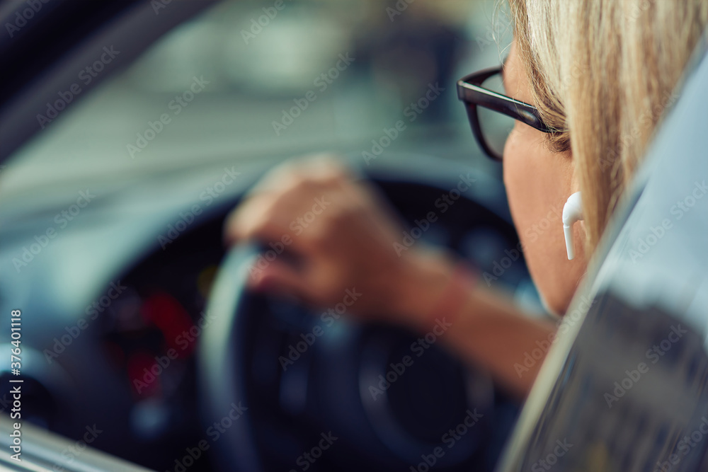 Close up shot of a woman wearing eyeglasses sitting behind steering wheel of her modern car, driving through the city