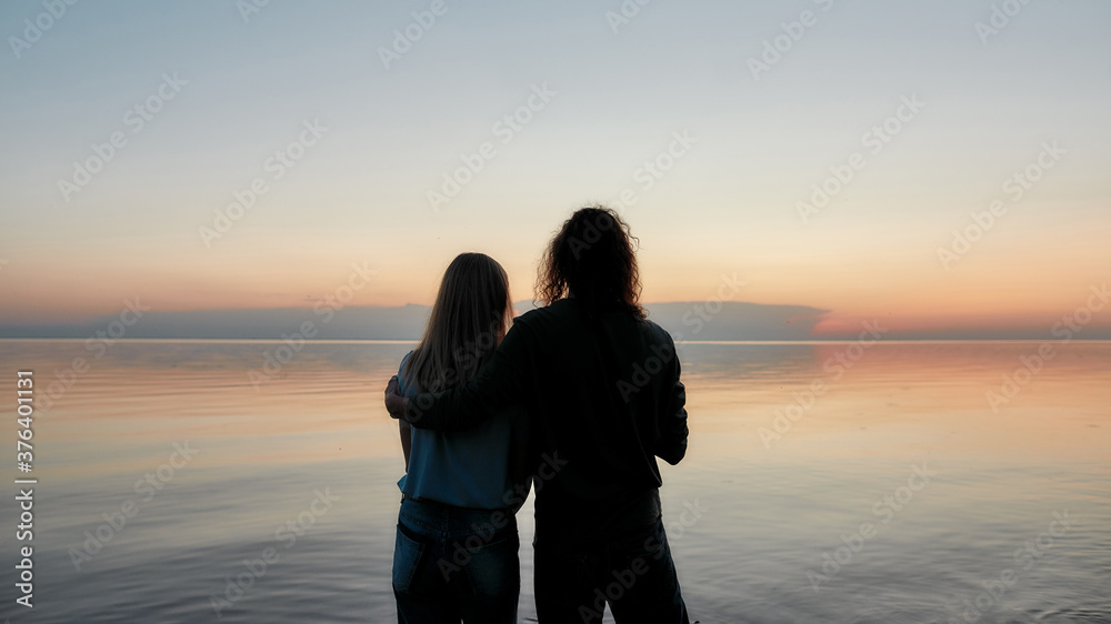 Silhouetted couple embracing while watching beautiful sunset on the river together