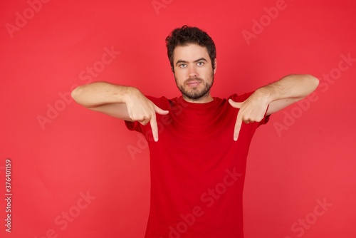 Young handsome caucasian man wearing t-shirt over isolated red background pointing with two fingers at copy space down. Place for advertising