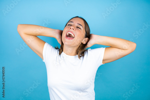 Young beautiful woman over isolated blue background relaxing and stretching, arms and hands behind head and neck smiling happy