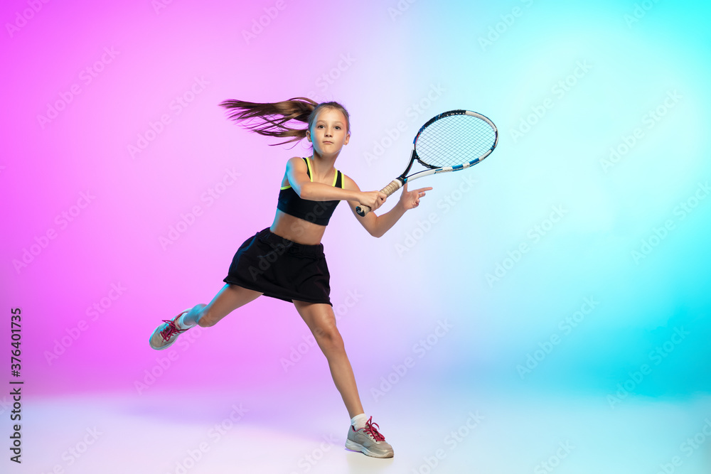 Aspiration. Little tennis girl in black sportwear isolated on gradient background in neon light. Little caucasian model, sport kid training in motion and action. Sport, movement, childhood concept.