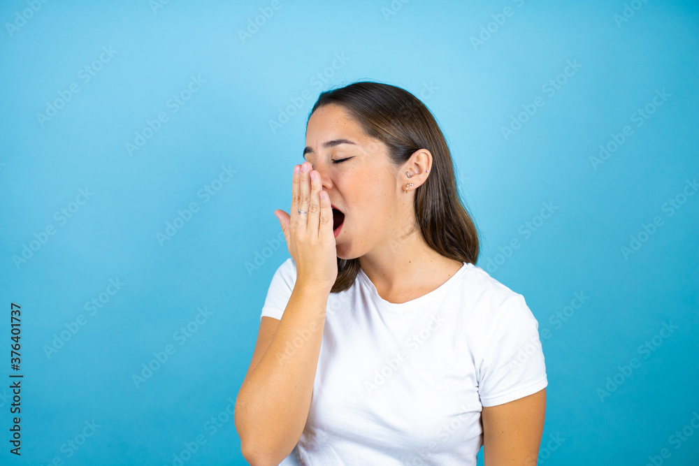 Young beautiful woman over isolated blue background bored yawning tired covering mouth with hand. Restless and sleepiness. Young beautiful woman over isolated blue background bored yawning tired covering mouth with hand. Restless and sleepiness.