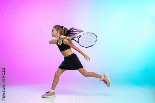 Unstoppable. Little tennis girl in black sportwear isolated on gradient background in neon light. Little caucasian model, sport kid training in motion and action. Sport, movement, childhood concept. © master1305