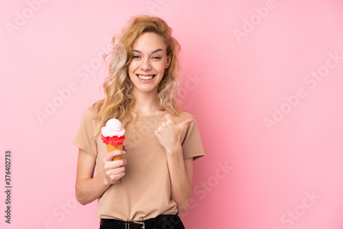 Young blonde woman holding a cornet ice cream isolated on pink background pointing to the side to present a product