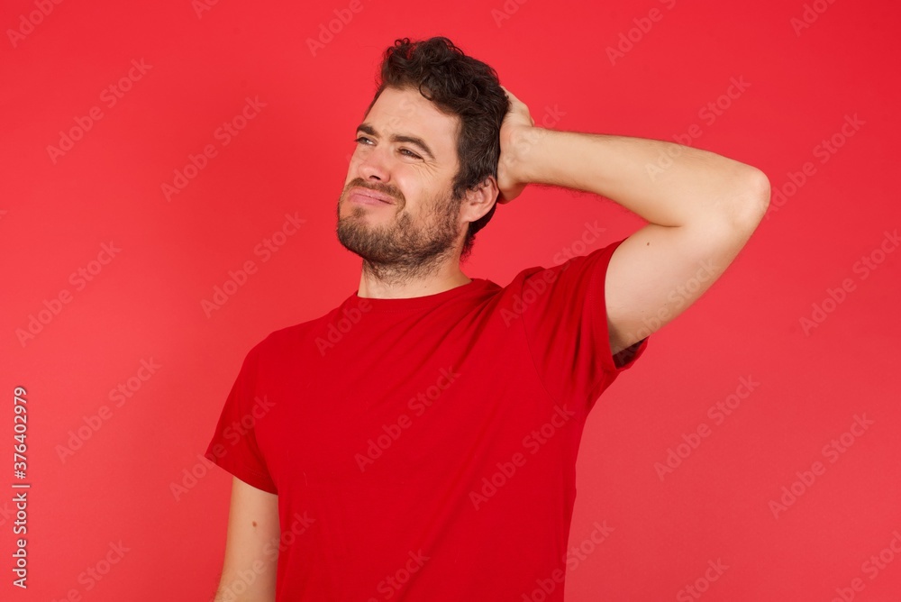 Young handsome caucasian man wearing t-shirt over isolated red background confuse and wonder about question. Uncertain with doubt, thinking with hand on head. Pensive concept. Young handsome caucasian man wearing t-shirt over isolated red background confuse and wonder about question. Uncertain with doubt, thinking with hand on head. Pensive concept.