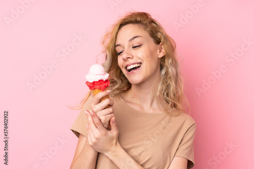 Young blonde woman holding a cornet ice cream isolated on pink background