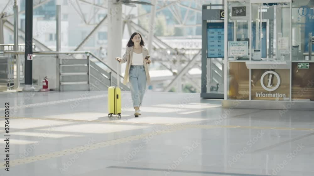 Portrait of beautiful young woman walking towards camera in airport terminal. Businesswoman looking around with amazed expression, walking with suitcase in hands in bright spacious building.
