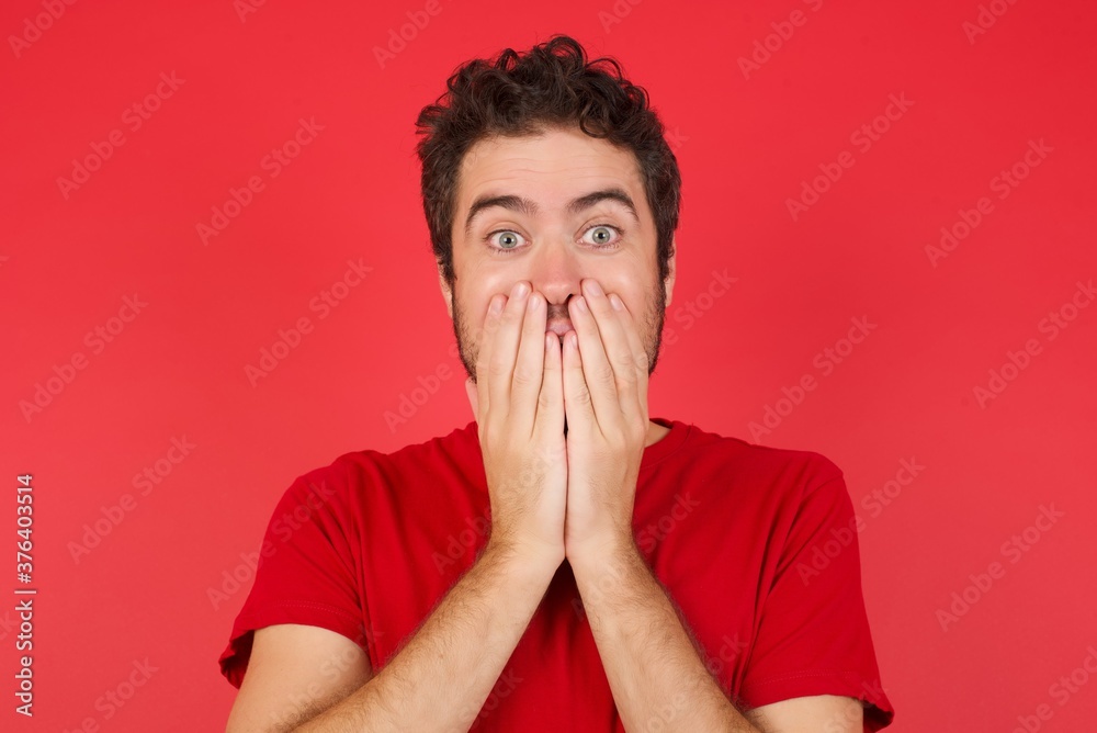 Vivacious Young handsome caucasian man wearing t-shirt over isolated red background, giggles joyfully, covers mouth, has fun alone, has natural laughter, hears positive story or funny anecdote Vivacious Young handsome caucasian man wearing t-shirt over isolated red background, giggles joyfully, covers mouth, has fun alone, has natural laughter, hears positive story or funny anecdote