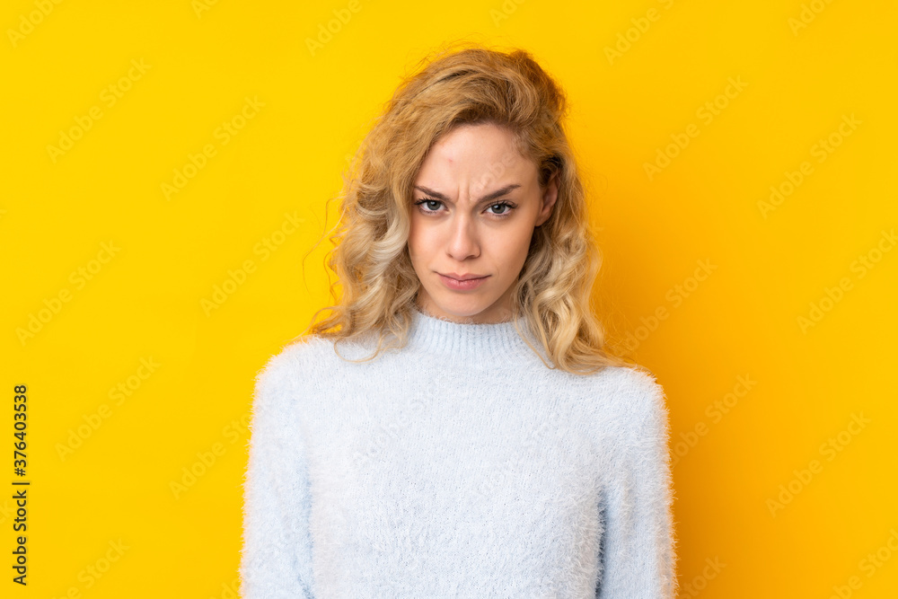 Young blonde woman isolated on yellow background with sad and depressed expression