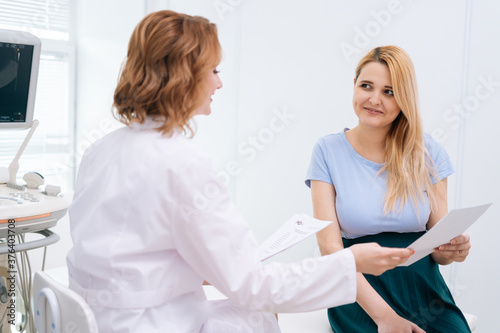 Female doctor transmits to young pregnant woman with blonde hair the results and reports of tests and conducted. Concept of happy and healthy childbearing.
