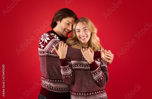 Beautiful romantic couple in Christmas sweaters embracing over red background