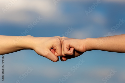 Two female hands doing fist bump over blue sky background © bander