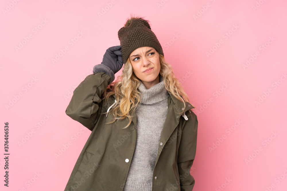Young girl with winter hat isolated on pink background having doubts and with confuse face expression Young girl with winter hat isolated on pink background having doubts and with confuse face expression