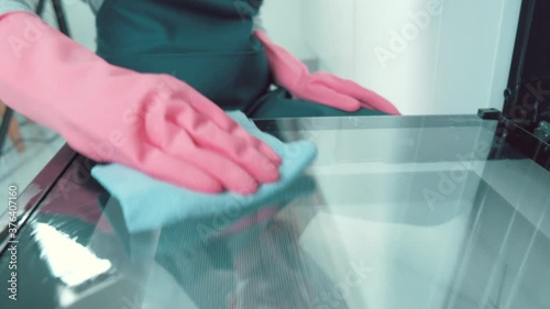 The girl wipes the kitchen door inside the oven with a rag. Girl in pink rubber gloves.