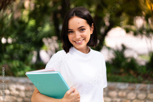 Young happy student woman holding notebooks at outdoors